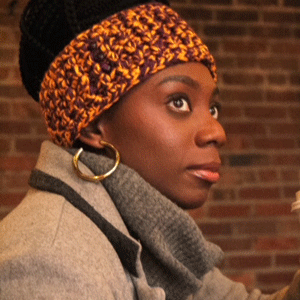 Girl wearing a handmade crocheted ear warmer or headband in the colors goldenrod yellow and violet purple. The headband has three small violet buttons sewn on the side.