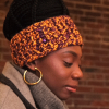 Girl wearing a handmade crocheted ear warmer or headband in the colors goldenrod yellow and violet purple. The headband has three small violet buttons sewn on the side.