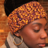 Girl wearing a handmade crocheted ear warmer or headband in the colors goldenrod yellow and violet purple. The headband has three small violet buttons sewn on the side.