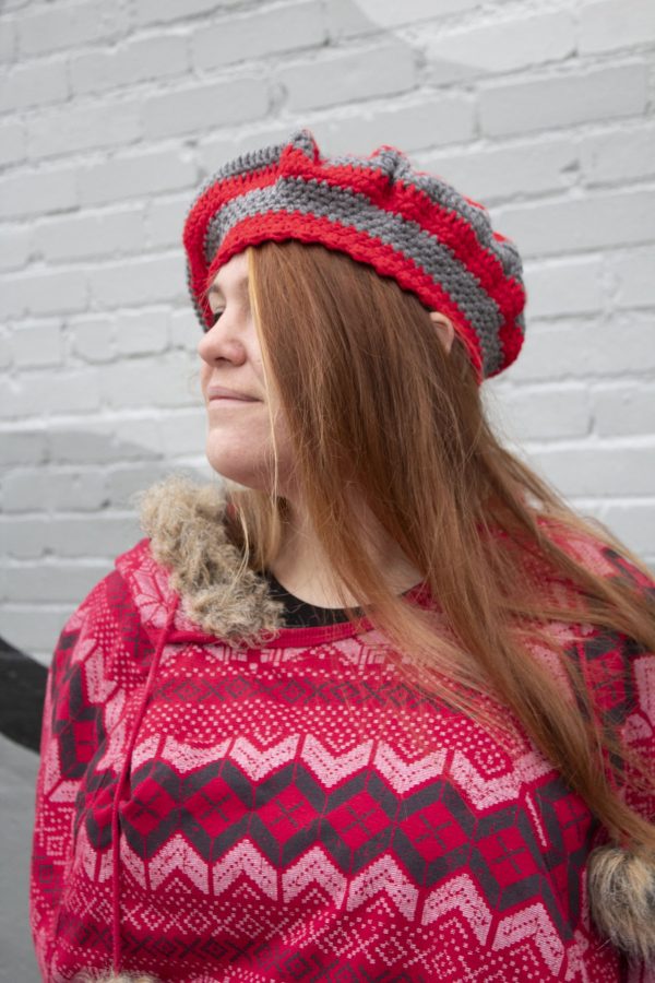 girl standing against a gray wall wearing a scarlet and gray tam with a grey pom pom