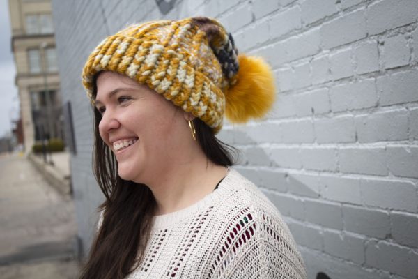 girl in handknit floppy golden yellow and navy blue toboggan. The toboggan has a pom pom at the end