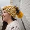 girl in handknit floppy golden yellow and navy blue toboggan. The toboggan has a pom pom at the end