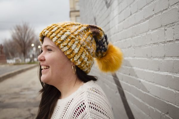 girl in handknit floppy golden yellow and navy blue toboggan. The toboggan has a pom pom at the end