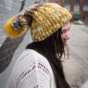 girl in handknit floppy golden yellow and navy blue toboggan. The toboggan has a pom pom at the end