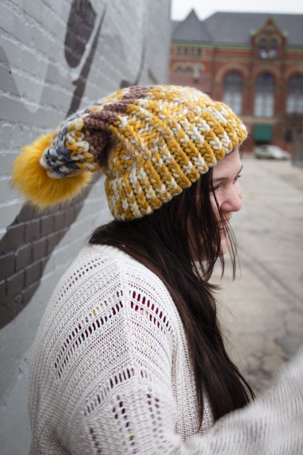 girl in handknit floppy golden yellow and navy blue toboggan. The toboggan has a pom pom at the end