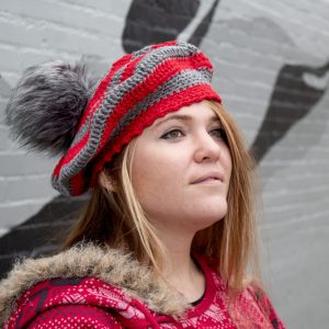 girl standing against a gray wall wearing a scarlet and gray tam with a grey pom pom