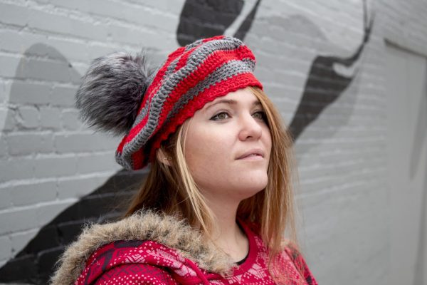 girl standing against a gray wall wearing a scarlet and gray tam with a grey pom pom