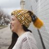girl in handknit floppy golden yellow and navy blue toboggan. The toboggan has a pom pom at the end