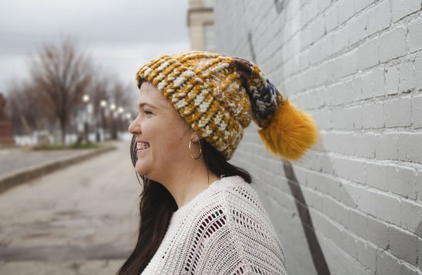 girl in handknit floppy golden yellow and navy blue toboggan. The toboggan has a pom pom at the end