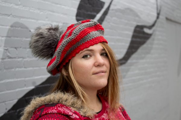 girl standing against a gray wall wearing a scarlet and gray tam with a grey pom pom