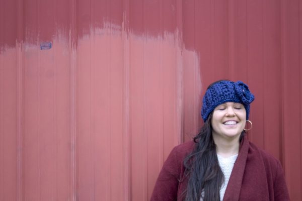 girl wearing a navy blue handmade crocheted headband or ear warmer. The ear warmer has a hand crocheted flower with a brown button center