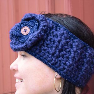 girl wearing a navy blue handmade crocheted headband or ear warmer. The ear warmer has a hand crocheted flower with a brown button center