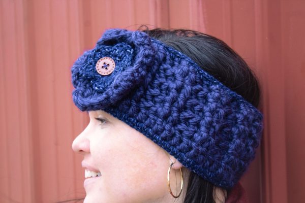 girl wearing a navy blue handmade crocheted headband or ear warmer. The ear warmer has a hand crocheted flower with a brown button center