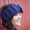 girl wearing a navy blue handmade crocheted headband or ear warmer. The ear warmer has a hand crocheted flower with a brown button center