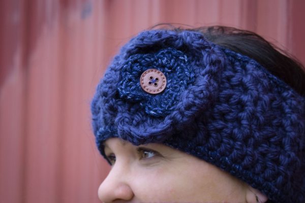 girl wearing a navy blue handmade crocheted headband or ear warmer. The ear warmer has a hand crocheted flower with a brown button center