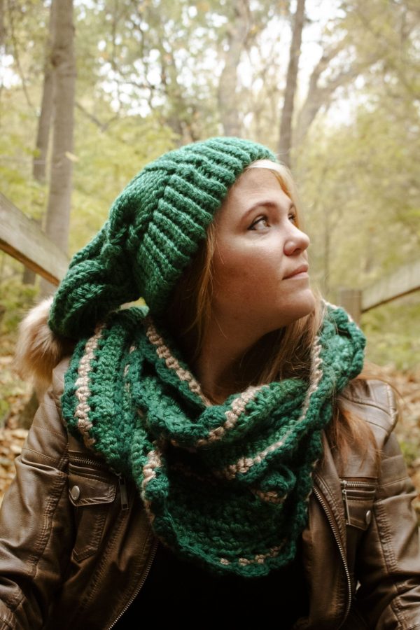 Girl sitting outside wearing a vibrant green floppy toboggan and infinity scarf matching set. The toboggan and scarf are handmade by MiasWorkshop. The hat is hand knit. The scarf is crocheted. The toboggan has a tan pom pom attached. The scarf has a matching tan stripe running through it.