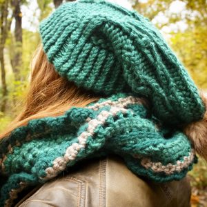 Girl outside wearing a vibrant green floppy toboggan and infinity scarf matching set. The toboggan and scarf are handmade by MiasWorkshop. The hat is hand knit. The scarf is crocheted. The toboggan has a tan pom pom attached. The scarf has a matching tan stripe running through it.