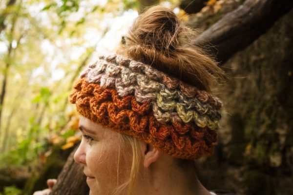 Girl wearing a handmade crocheted ear warmer or headband in the colors dark orange, peach, cream and light brown. Crocodile stitch