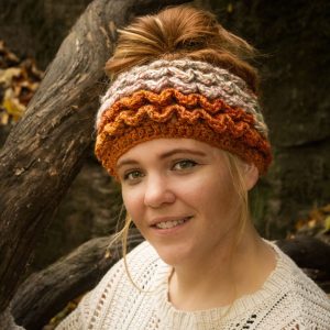 Girl wearing a handmade crocheted ear warmer or headband in the colors dark orange, peach, cream and light brown. Crocodile stitch