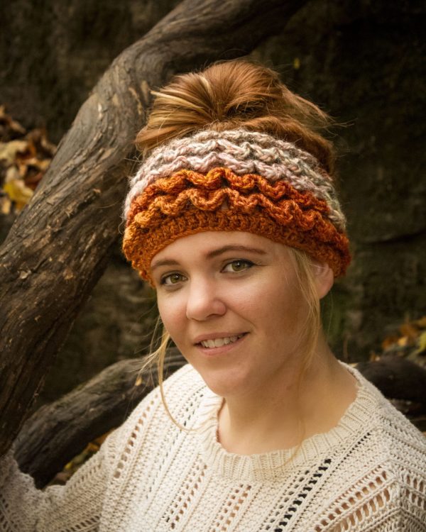 Girl wearing a handmade crocheted ear warmer or headband in the colors dark orange, peach, cream and light brown. Crocodile stitch