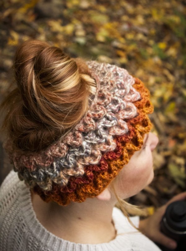 Girl wearing a handmade crocheted ear warmer or headband in the colors dark orange, peach, cream and light brown. Crocodile stitch