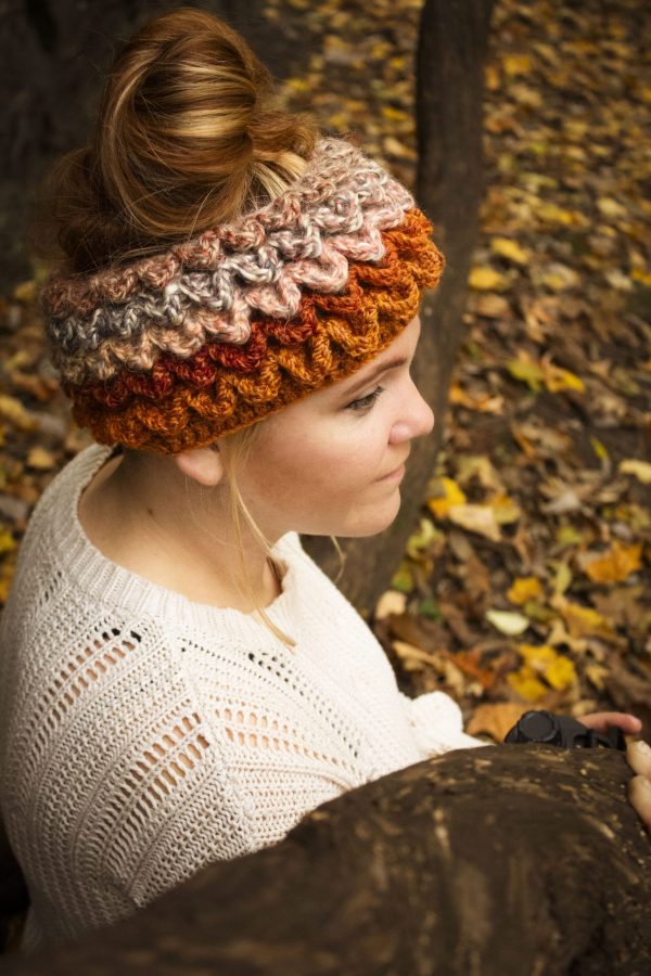 Girl wearing a handmade crocheted ear warmer or headband in the colors dark orange, peach, cream and light brown. Crocodile stitch