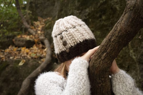 girl wearing a fuzzy cream and dark brown hand crocheted beanie with three coconut buttons sewn on the side