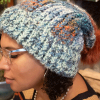 girl wearing a handmade knit slouchy toboggan. The toboggan is blue, green, cram, and orange, and it has a matching orange pom pom