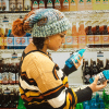 girl standing in store wearing a handmade knit slouchy toboggan. The toboggan is blue, green, cram, and orange, and it has a matching orange pom pom