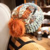 girl wearing a handmade knit slouchy toboggan. The toboggan is blue, green, cram, and orange, and it has a matching orange pom pom
