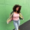 girl with curly hair against a green background wearing a pink and green granny square sweater with roses on the sleeves. The sweater zips in the front and has pockets