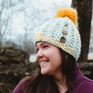 Handmade, crocheted, seafoam green and goldenrod yellow beanie with golden yellow pom pom and three coconut buttons sewn onto the side