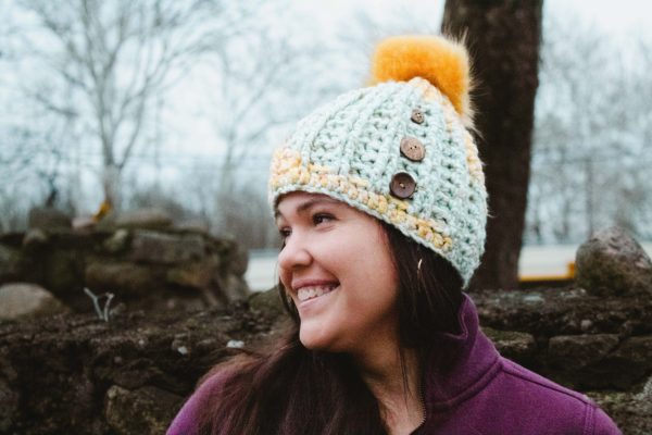 Handmade, crocheted, seafoam green and goldenrod yellow beanie with golden yellow pom pom and three coconut buttons sewn onto the side