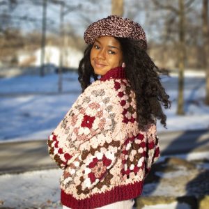 a girl standing outside in a pink, dark red, dark brown, and cream granny square sweater. The sweater buttons up the front. MiasWorkshop