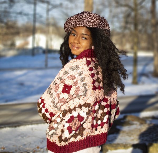 a girl standing outside in a pink, dark red, dark brown, and cream granny square sweater. The sweater buttons up the front. MiasWorkshop