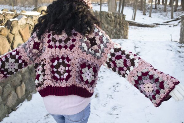 a girl standing outside in a pink, dark red, dark brown, and cream granny square sweater. The sweater buttons up the front. MiasWorkshop