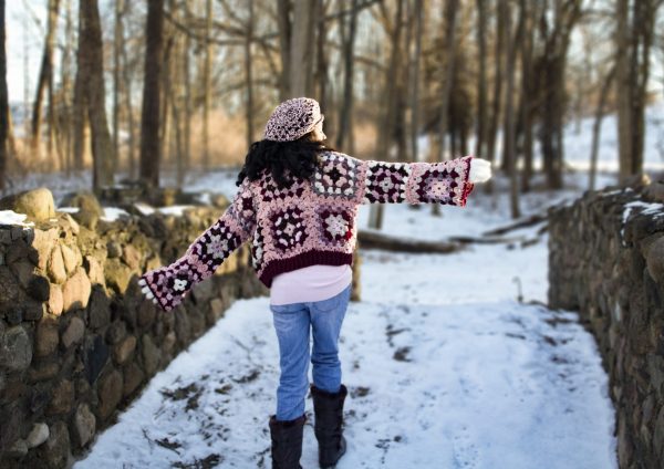 a girl standing outside in a pink, dark red, dark brown, and cream granny square sweater. The sweater buttons up the front. MiasWorkshop