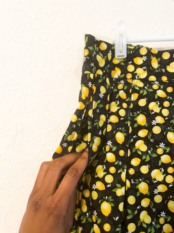 Up close photo of the pocket on a lemon pattern pleated skirt with black background. Has zipper closure. 30 1/2 inch waist. Length of skirt is 27 inches