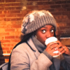girl in a coffee shop wearing a handmade, knit, slouchy, fuzzy, cream and gray checkered toboggan with a gray pom pom attached