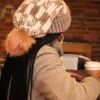 girl in a coffee shop wearing a handmade, knit, slouchy, fuzzy, cream and gray checkered toboggan with a gray pom pom attached